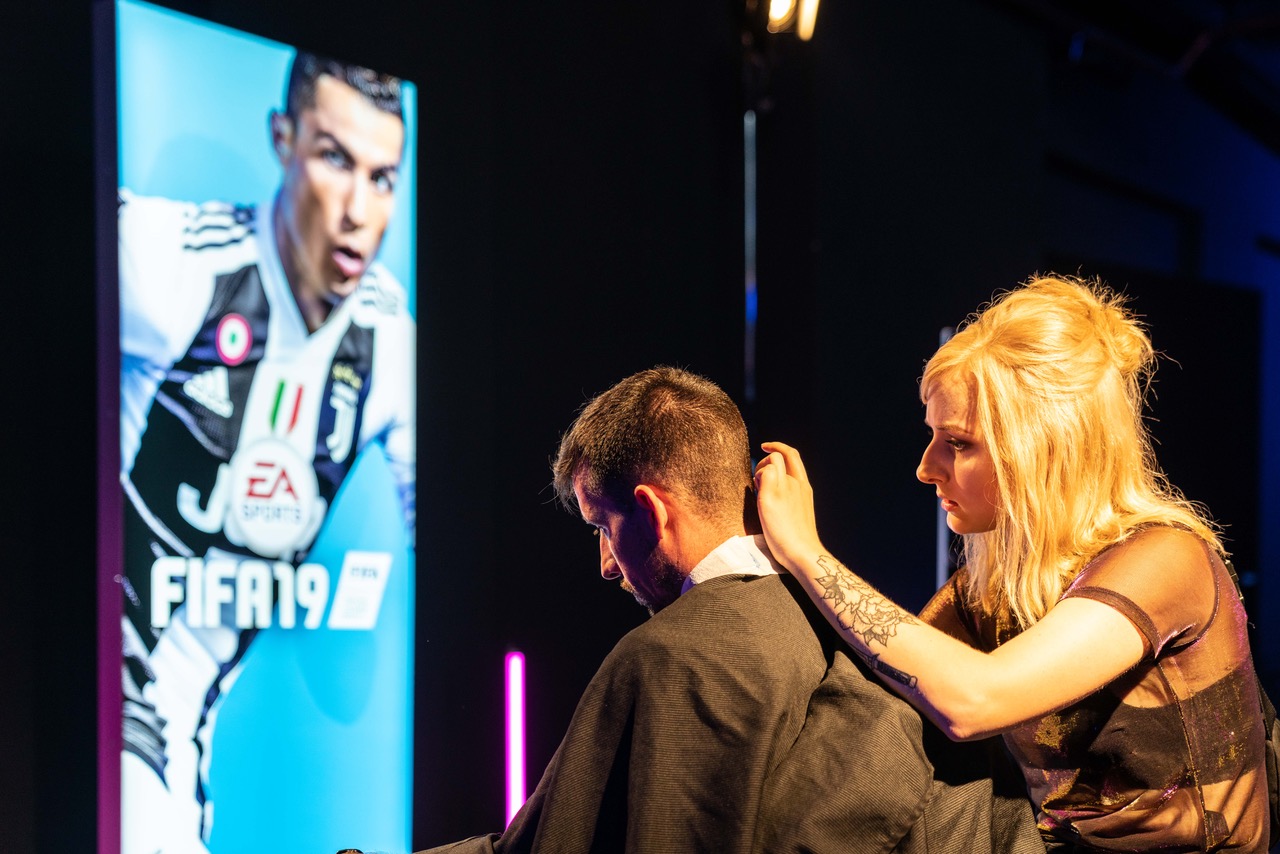 Eine Friseurin schneidet einem Gast die Haare und im Hintergrund steht ein Fifa 19 Branding
