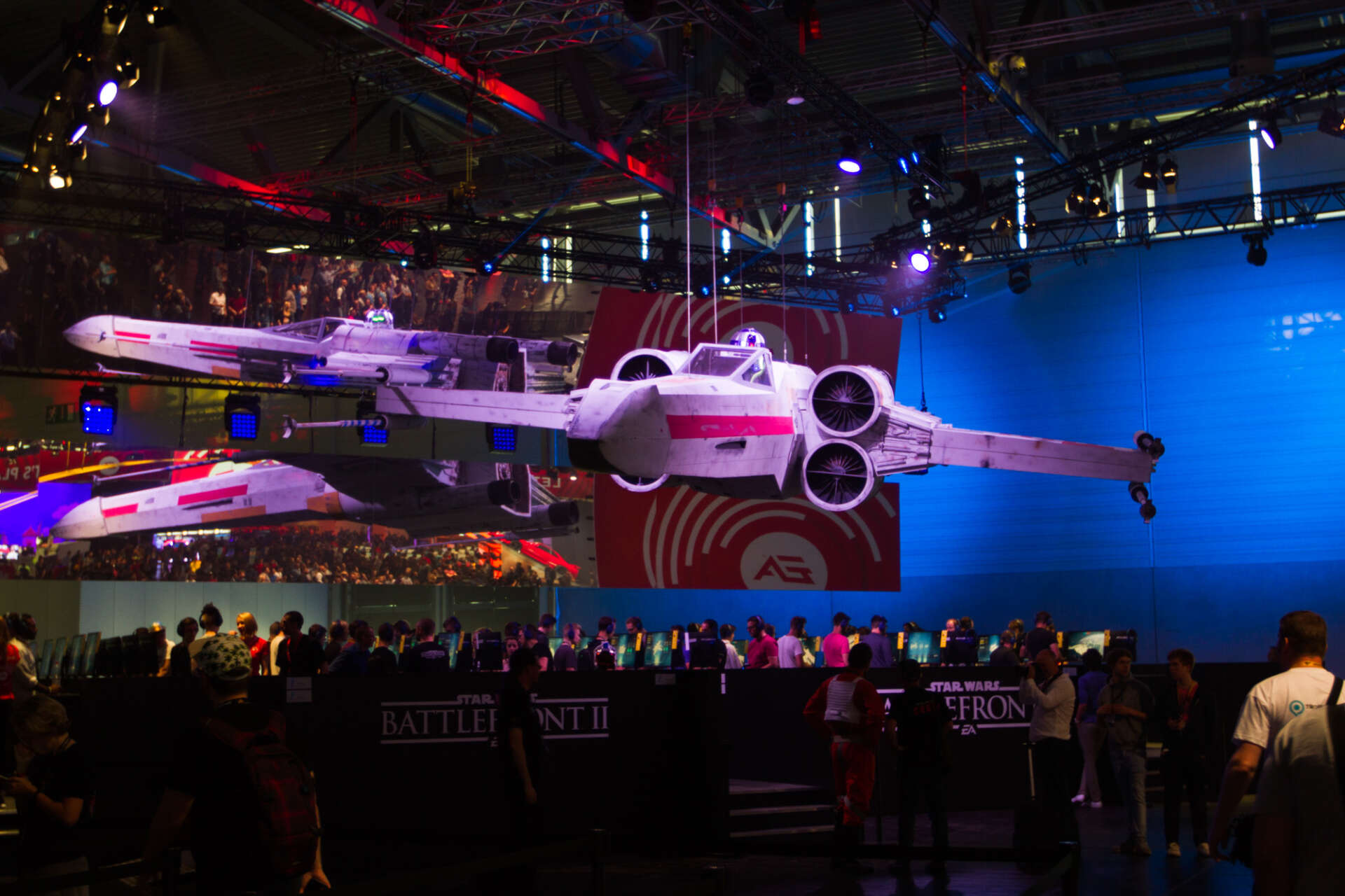 Ein Star Wars Raumschiff haengt an Seilen über den Anspielstationen und dem Publikum von Battlefront II
