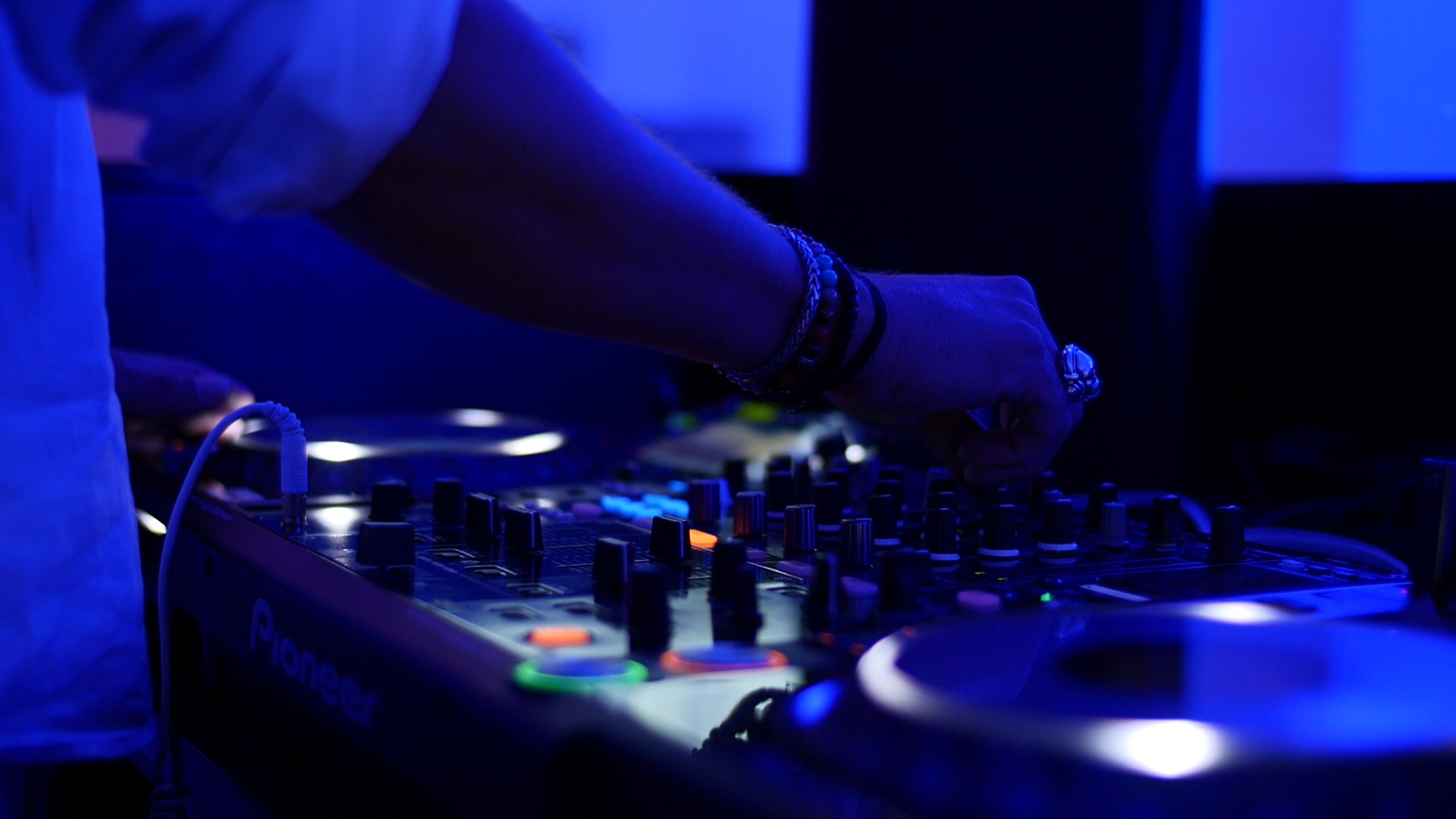 Man sieht ein DJ-Pult und die Hände des DJs bei Party-Beleuchtung